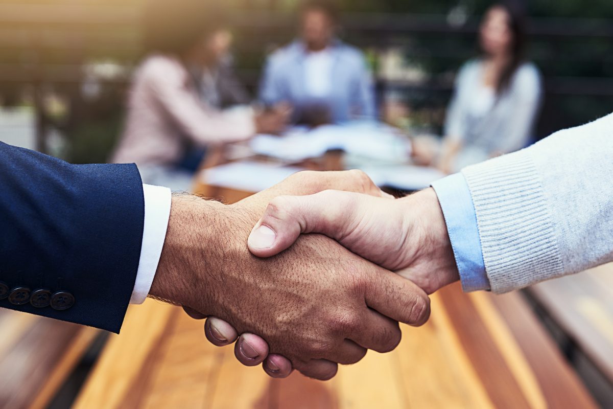 Closeup shot of two unrecognizable businessmen shaking hands with their colleagues in the background.